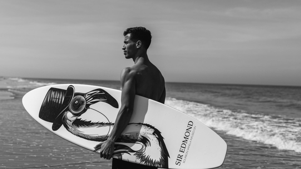 Image of a man with a Sir Edmond gin branded surfboard.